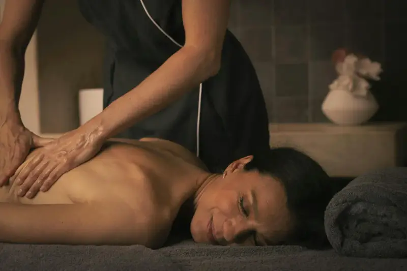 Mani esperte eseguono uno dei tanti tipi di massaggi, rilassando la schiena di una donna in un'atmosfera serena.