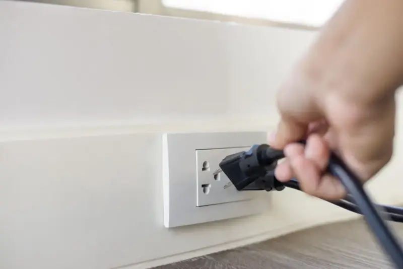 Main d'une personne branchant un appareil sur une prise murale. Une solution simple pour installer une prise électrique sans percer.