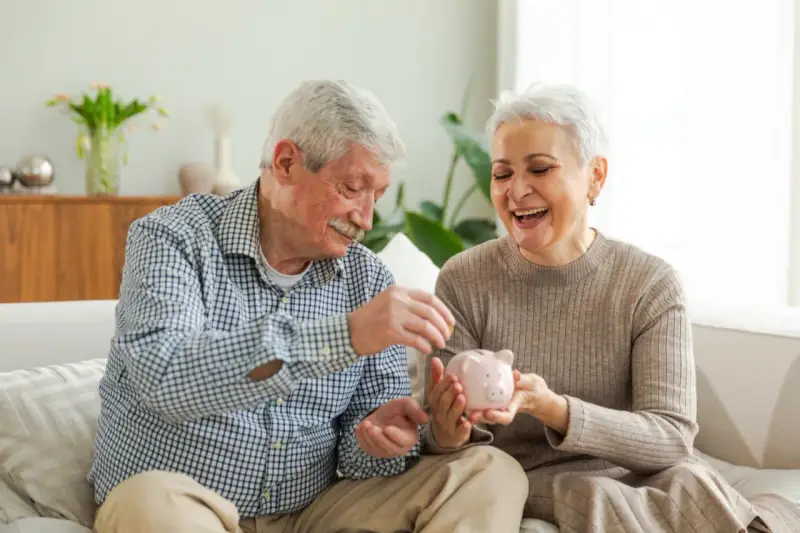 Szczęśliwa para seniorów wrzuca monety do świnki-skarbonki, planując spokojne przejście na emeryturę.