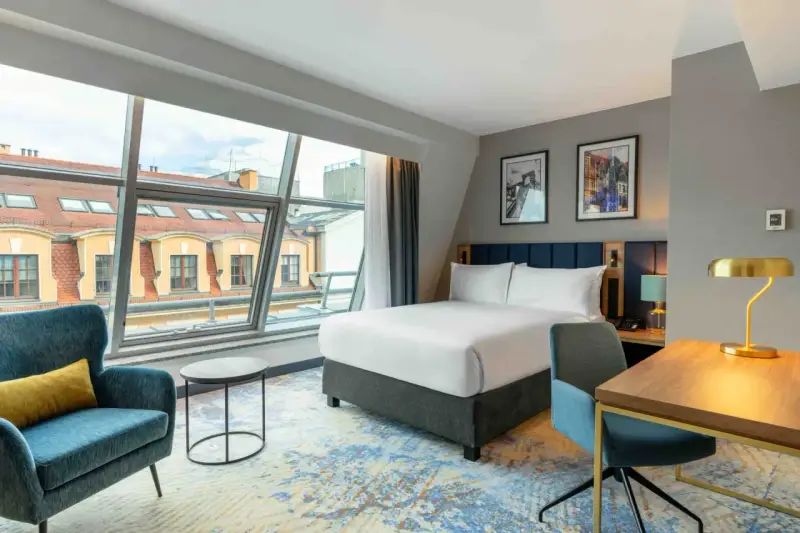 Nowoczesny pokój hotelowy z dużym oknem i widokiem na dachy. Czy zeby zarezerwowac hotel ttzna miec 18 lat? Tak, zazwyczaj.