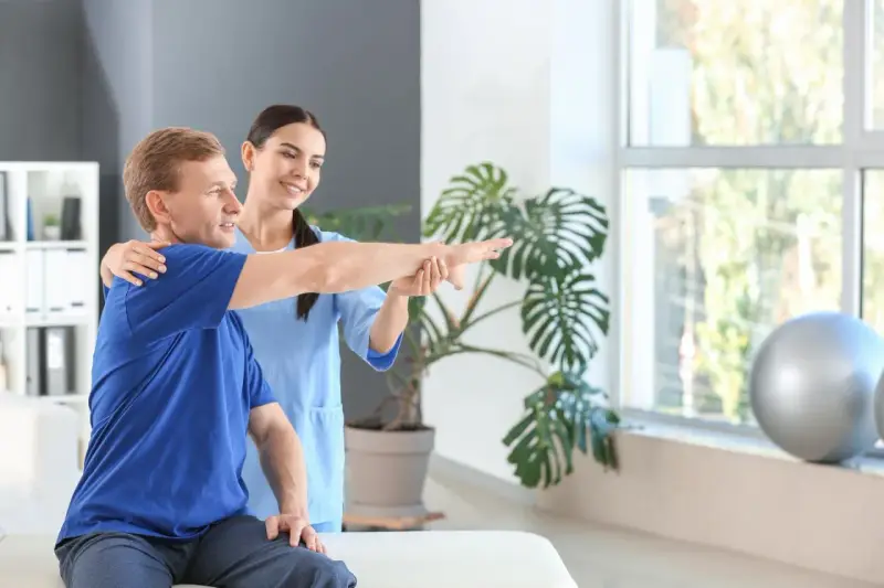 Ein Physiotherapeut unterstützt einen Patienten bei der Armbewegung.