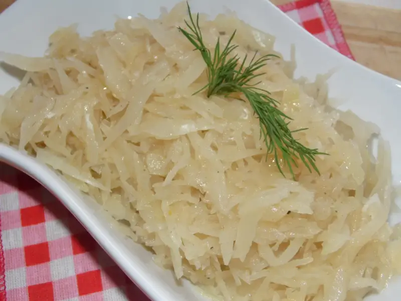 Gotowana biała kapusta do obiadu, podana w białej misce, ozdobiona gałązką koperku.