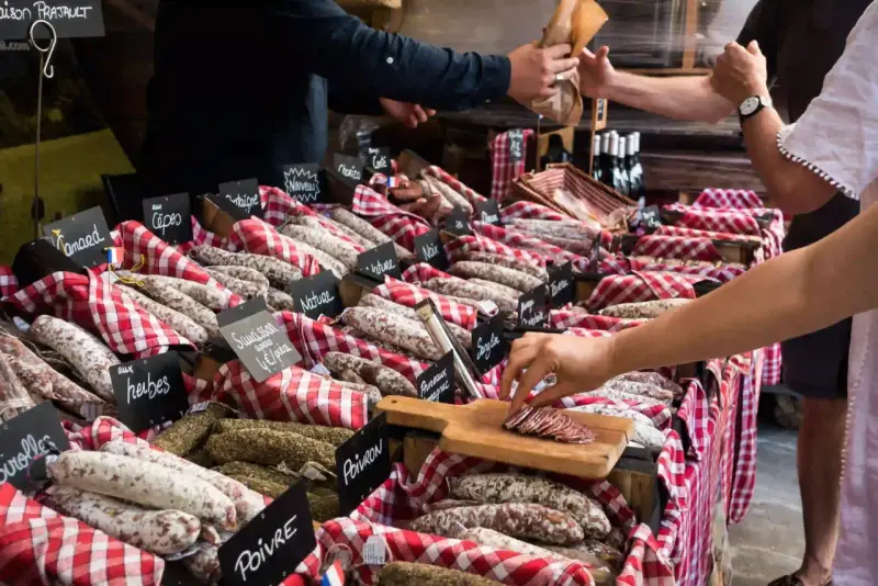 Vitrine de charcuterie avec de nombreuses saucisses et un client qui en choisit une tranche.