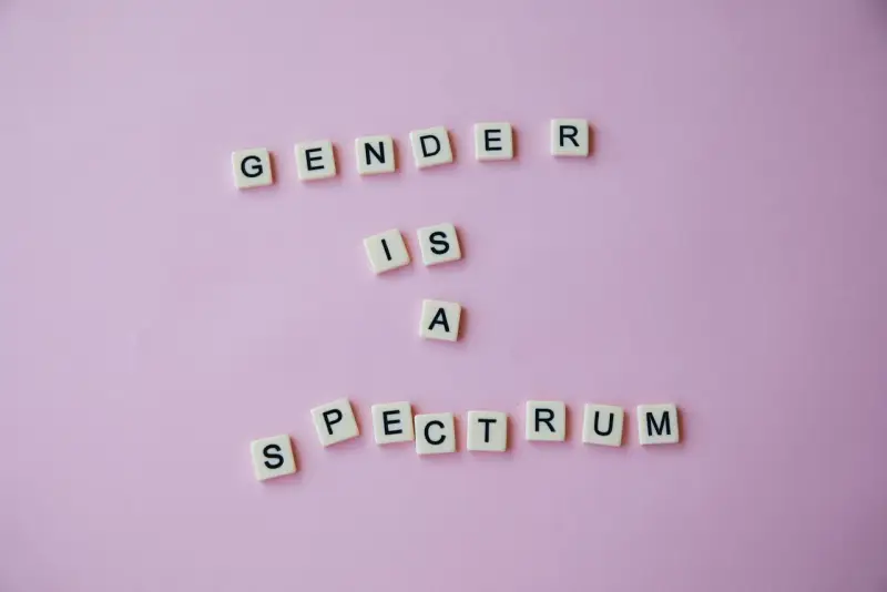 Litery na różowym tle układają się w napis "GENDER IS A SPECTRUM". To przypomnienie, że tożsamość płciowa nie jest binarna, a doświadczenie dysforii płciowej jest częścią tej złożoności.