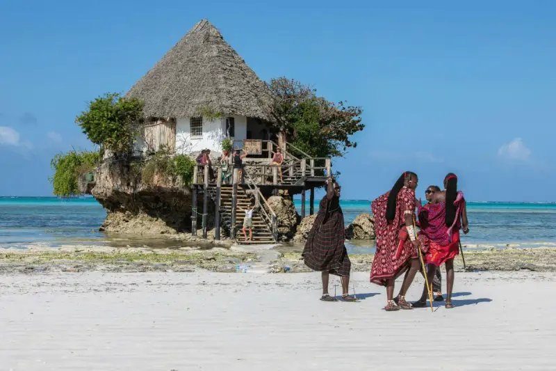 Wspaniały marzec na Zanzibarze. Ludzie w tradycyjnych strojach spacerują po plaży przy restauracji "The Rock" na skale.