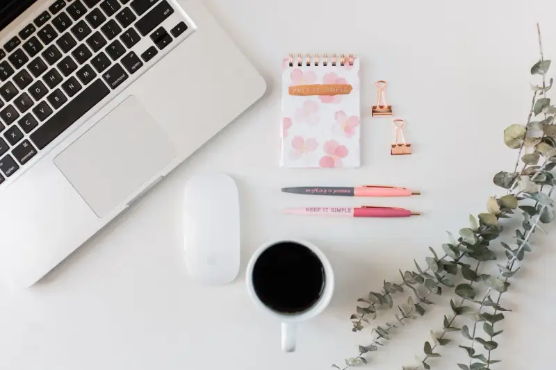 Ein Schreibtisch mit Laptop, Maus, Notizbuch, Stiften und Kaffee. Ideal für Lehrer, die ihr Zeitmanagement verbessern wollen.