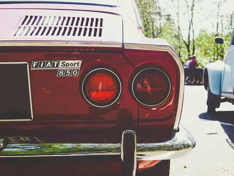Dettaglio posteriore di una Fiat Sport 850 rossa, con i suoi iconici fanali rotondi. Un pezzo di storia automobilistica, un vero art 102 cds.
