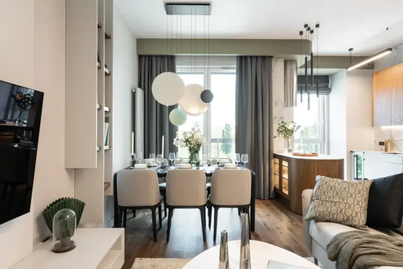 Elegancka jadalnia z nowoczesnym stołem i krzesłami. W tle kuchnia z drewnianymi elementami i subtelnym akcentem w kolorze pistacjowym.