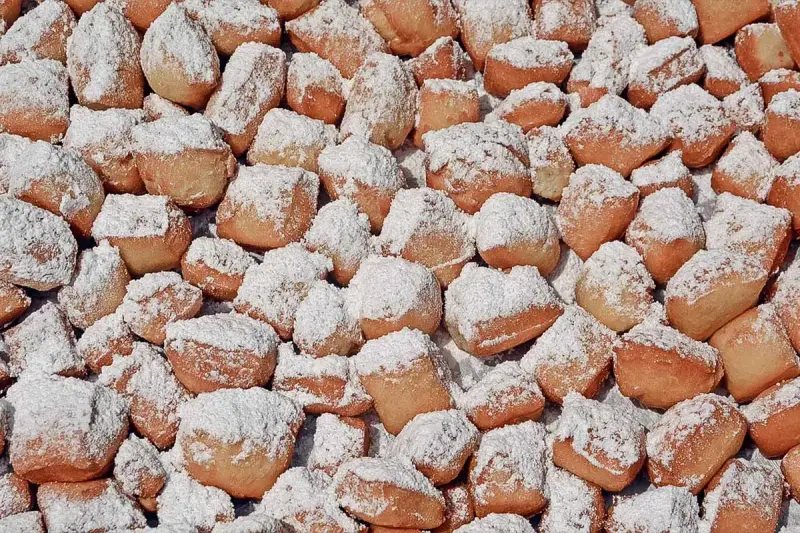 Ein Haufen goldbrauner, puderzuckerbestäubter Schmalzkuchen, die an ein schmalzkuchen originalrezept erinnern.
