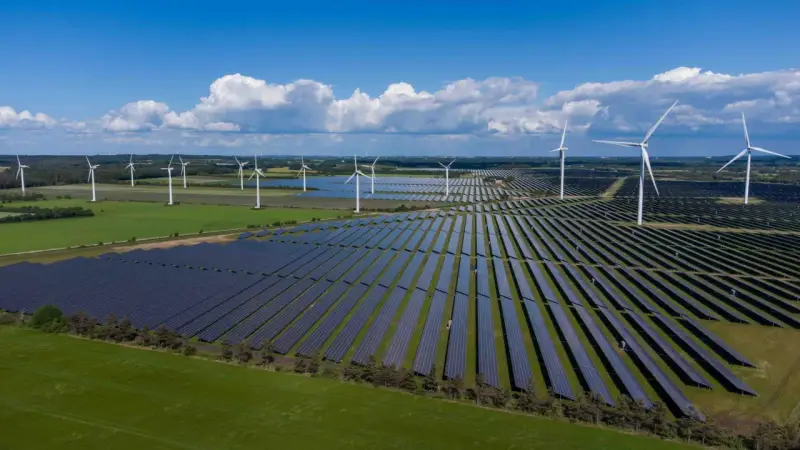 Großes Feld mit Windkraftanlagen und Photovoltaik-Modulen unter blauem Himmel mit Wolken.