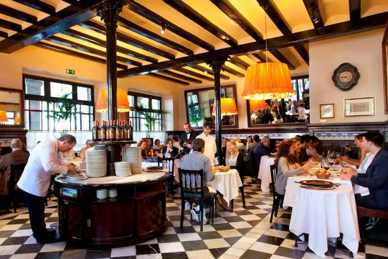 Un camarero prepara platos en un restaurante lleno de comensales. Los pasos para abrir un restaurante incluyen crear un ambiente acogedor como este.