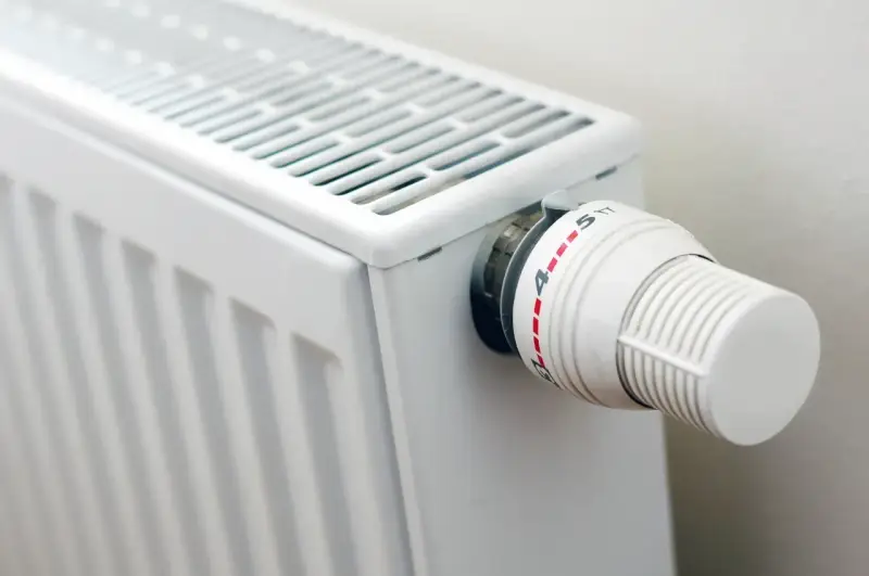 Biały grzejnik z termostatem. Różne rodzaje grzejników oferują różne sposoby regulacji temperatury.