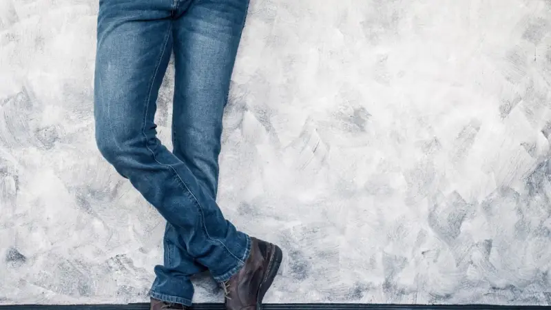 Mężczyzna w jeansach H&M, stojący przy ścianie. Rozmiarówka H&M wypada standardowo, idealnie dopasowana.