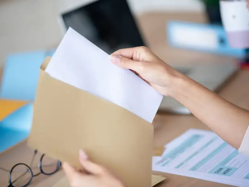 Dłoń wkłada biały papier do brązowej koperty. Wzór adresowania koperty A4 jest gotowy do wypełnienia.