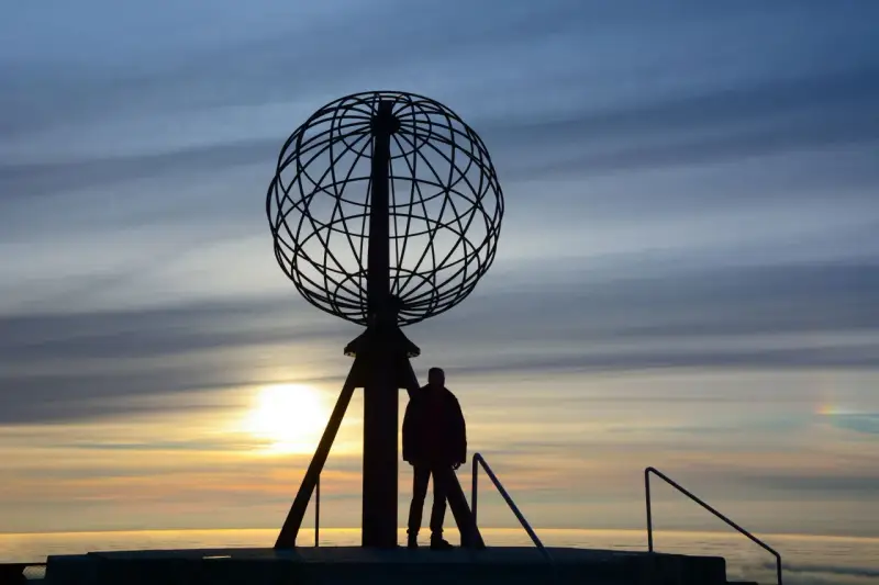 Sylwetka człowieka przy globusie na Nordkapp podczas zachodu słońca.