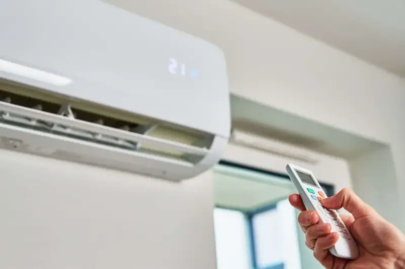 Mano ajustando el aire acondicionado a la temperatura ideal para ahorrar energía. La unidad muestra 21 grados.