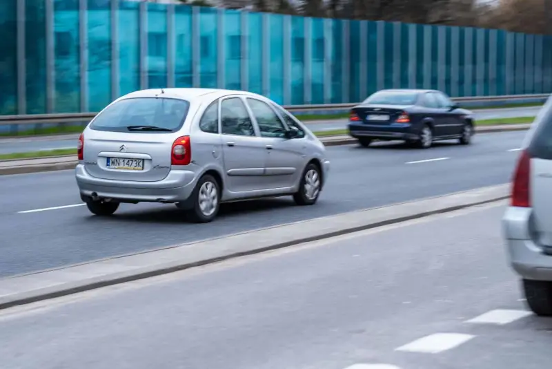 Srebrny Citroën Xsara Picasso jedzie po drodze, mijając inne samochody.