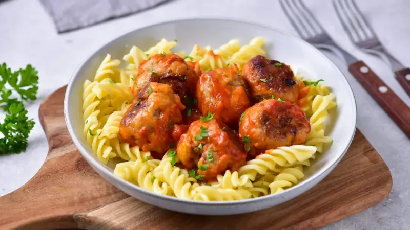 Pulpety w sosie pomidorowym jak u babci, podane z makaronem fusilli. Danie ozdobione posiekaną natką pietruszki.