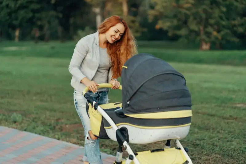 Mama z rudymi włosami uśmiecha się do wózka. Idealny przykład, jak ubrać noworodka na spacer 15 stopni.