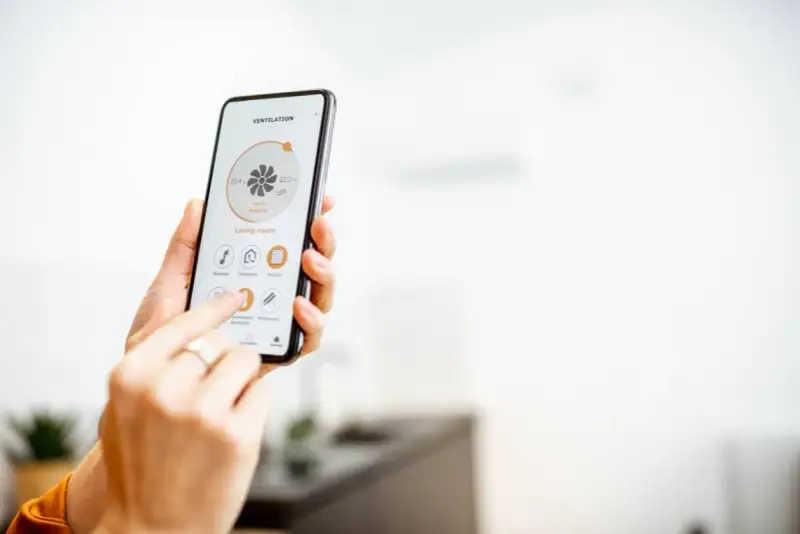 Mano usando un smartphone para encender calefacción a distancia en la sala de estar.