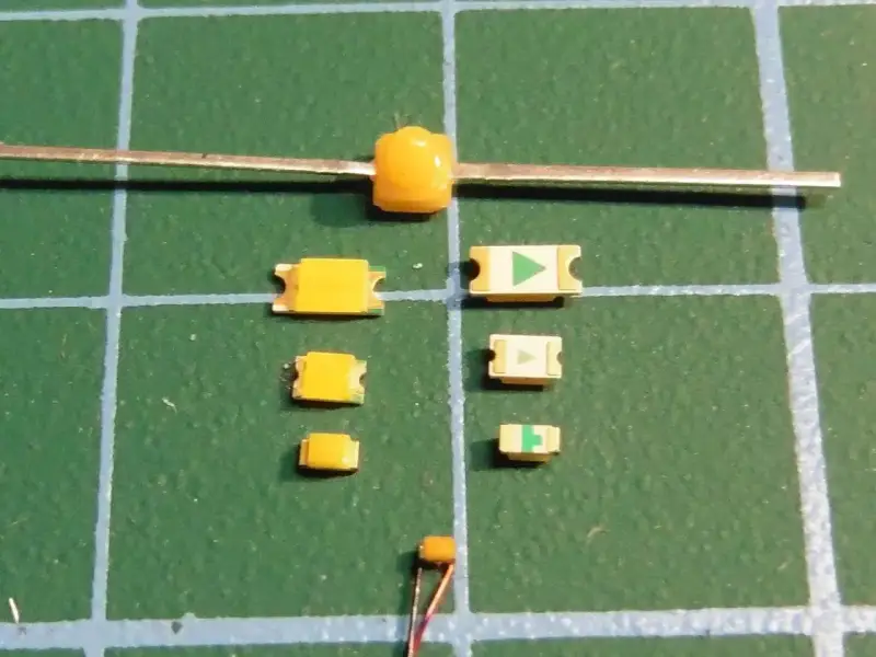 Mehrere kleine gelbe LEDs liegen auf einer grünen Schneidematte. Eine größere gelbe LED ist an einem Metallstift befestigt.