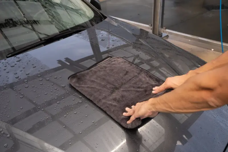 Hände trocknen mit einem Mikrofasertuch die Motorhaube nach der Autowäsche. Perfekt für das auto innenraum trocknen.