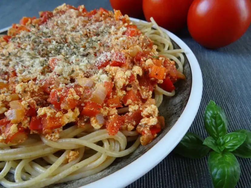 Talerz spaghetti z sosem pomidorowym i tofu, posypany serem i ziołami.