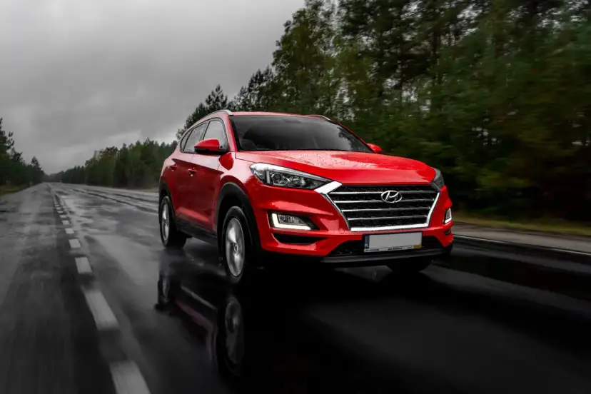 Czerwony Hyundai Tucson jedzie po mokrej drodze w deszczowy dzień. Warto pamiętać o filtrze CPL, którego zastosowanie poprawia widoczność w takich warunkach.