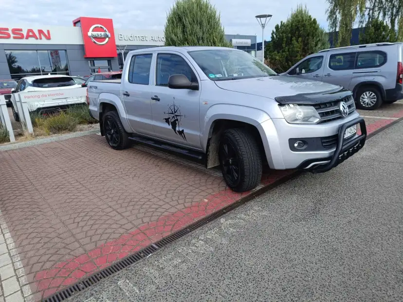 Srebrny pickup z naklejką kompasu i postacią, gotowy do podróży. Idealny do pkd wynajem samochodów.