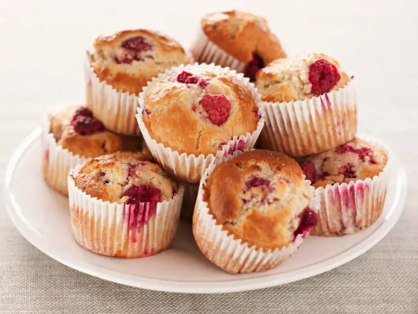 Stos muffinek z malinami na białym talerzu.