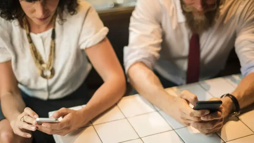 Zwei Personen sitzen an einem Tisch und schauen auf ihre Smartphones.
