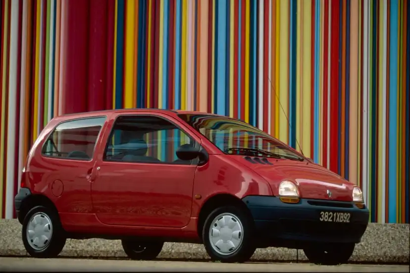 Renault Twingo 1 rouge devant un mur de bandes colorées verticales.