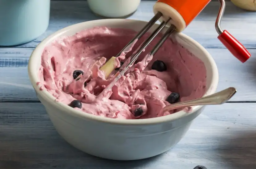 Różowy mus jagodowy do tortu, przygotowywany mikserem, z widocznymi całymi jagodami.