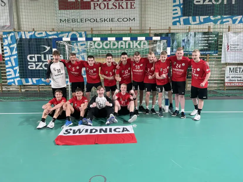 Drużyna piłki ręcznej z numerami na koszulkach, w tym Damian Borkowski, świętuje zwycięstwo.
