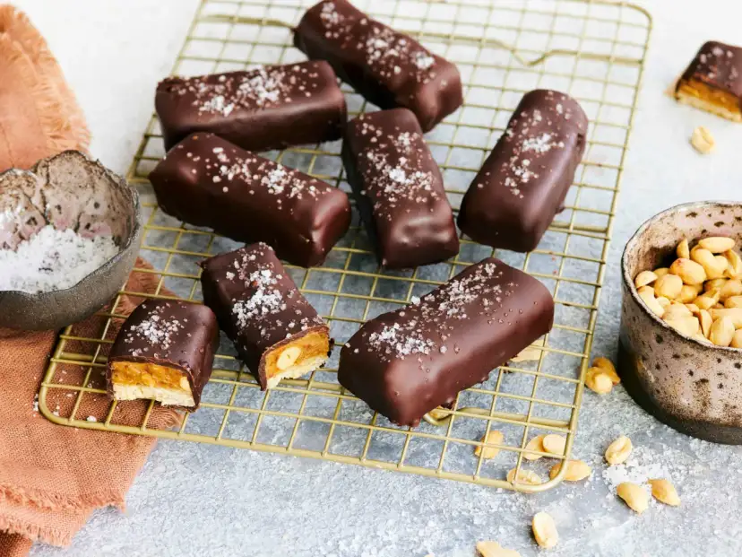 Vegane Snickers mit Karamell, Erdnüssen und Meersalz bestreut, auf einem goldenen Gitter.