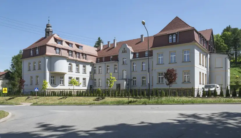 Elegancki budynek z wieżyczką, gdzie mieści się dom seniora Magda lenka, otoczony zielenią.