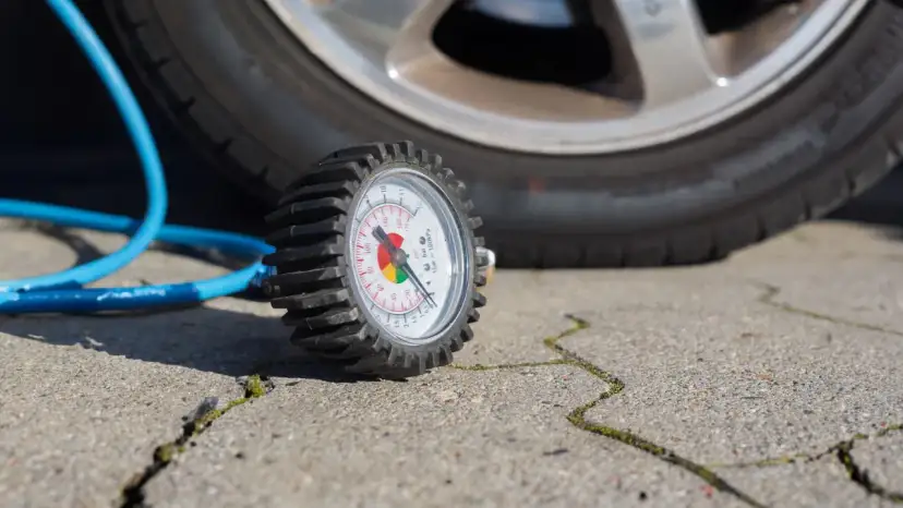 Manomètre de pression des pneus à côté d'une roue de voiture et d'un tuyau bleu.