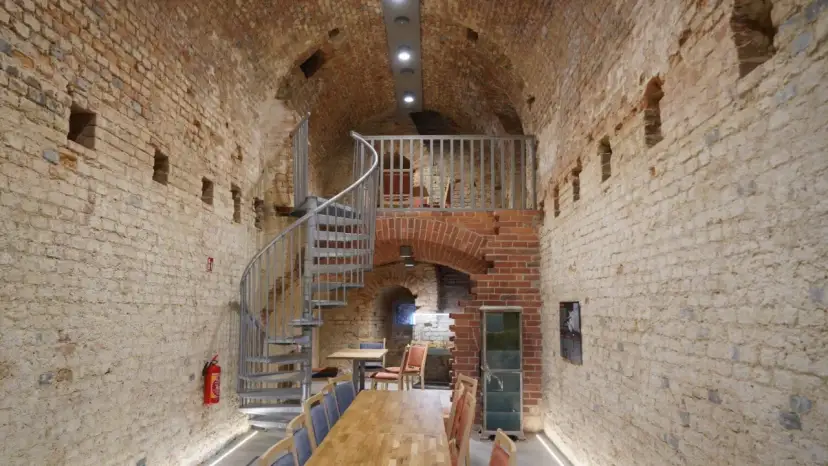 Wnętrze restauracji Srebrna Góra z kamiennymi ścianami, kręconymi schodami i drewnianymi stołami.