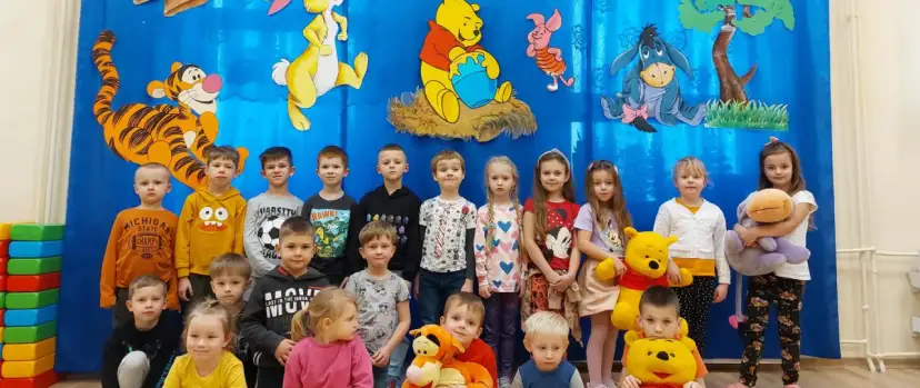 Dzieci pozują do zdjęcia z Kubusiem Puchatkiem i przyjaciółmi, świętując Dzień Kubusia Puchatka.