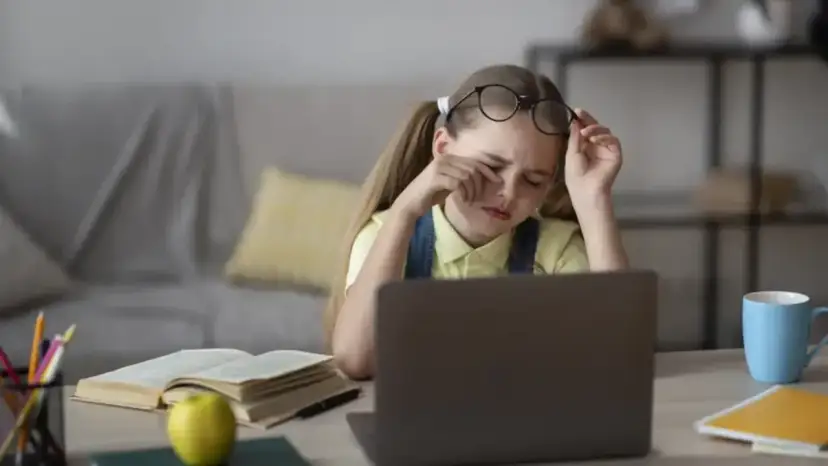 Zmęczona dziewczynka z okularami na czole pociera oczy, ucząc się przy laptopie. Jej indywidualna ścieżka nauczania jest trudna.