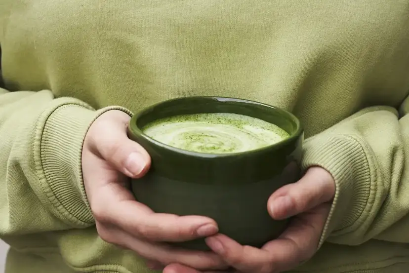 Dłonie trzymające zieloną miseczkę z pianką matcha.