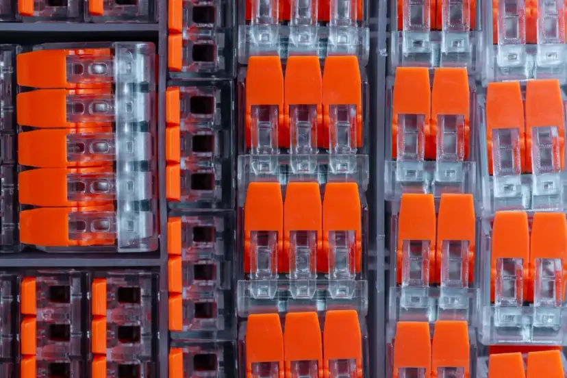 Zbliżenie na pomarańczowe złącza elektryczne w przezroczystych obudowach, ułożone w rzędy.