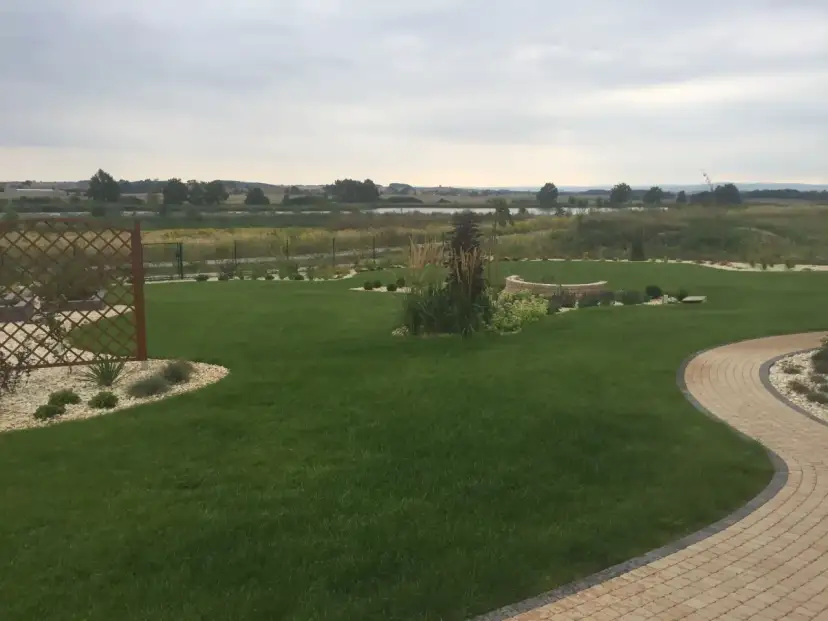 Zadbany ogród z trawnikiem, kamiennymi ścieżkami i rabatami. W tle jezioro i pola. Fosforan monopotasowy pomógł uzyskać tak piękny, zielony trawnik.