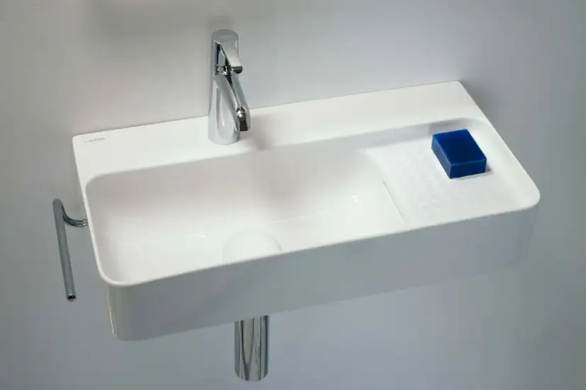 Elegancka, mała umywalka wisząca z chromowaną baterią i kostką niebieskiego mydła.