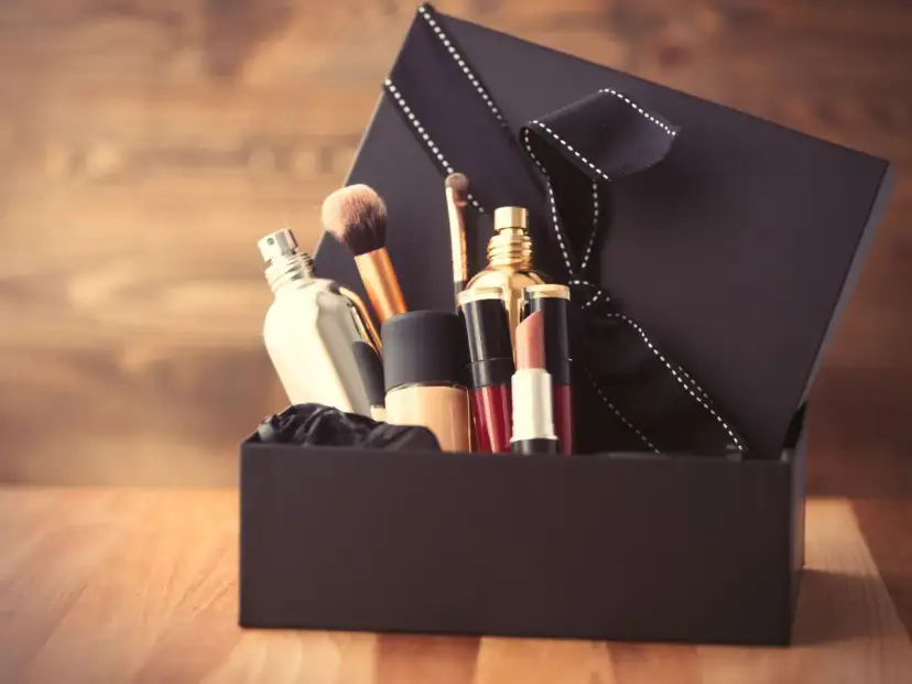 Schwarze Geschenkbox mit Kosmetikartikeln wie Parfüm, Lippenstift und Make-up-Pinseln.