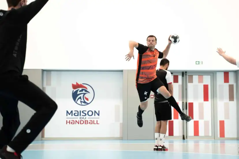 Piłkarz ręczny, niczym szczypiornista, wyskakuje do rzutu. W tle logo "Maison du Handball".