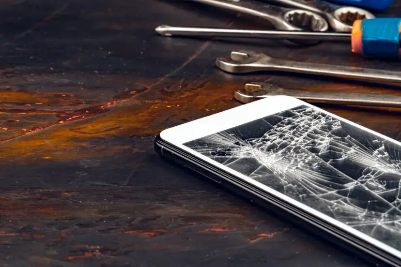 Zepsuty ekran telefonu leży obok narzędzi. Pęknięcia tworzą pajęczynę na szkle.