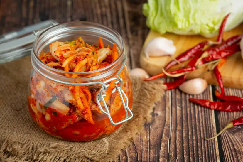 Słoik z kimchi na tle desek, z kapustą, czosnkiem i papryczkami chili.
