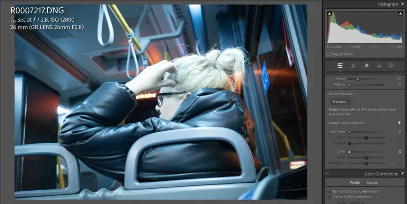 Kobieta w czarnej kurtce siedzi w autobusie, poprawiając włosy. Widać suwaki redukcji szumów w programie do edycji zdjęć.