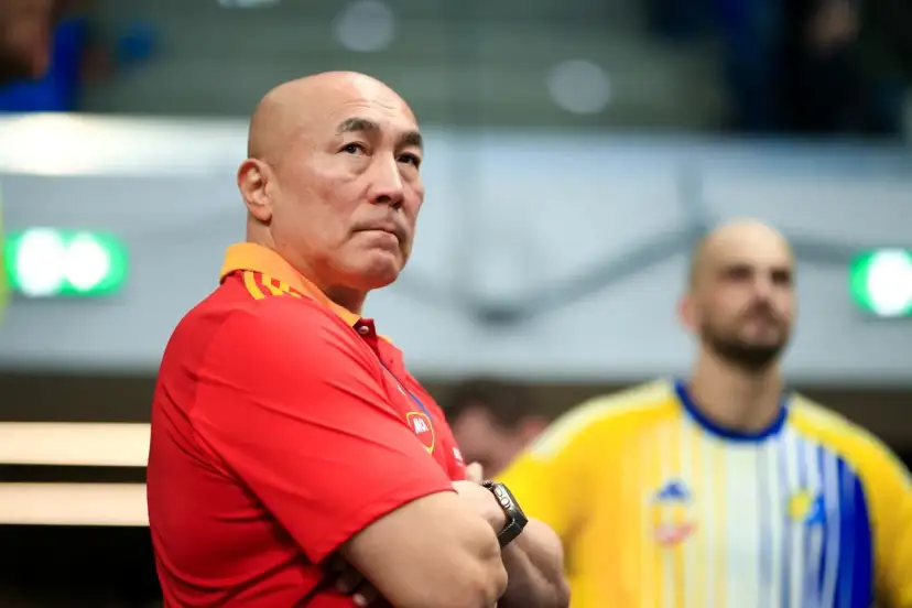 Skupiony trener Vive Kielce w czerwonej koszulce z pomarańczowym kołnierzem, z rękami skrzyżowanymi na piersi.